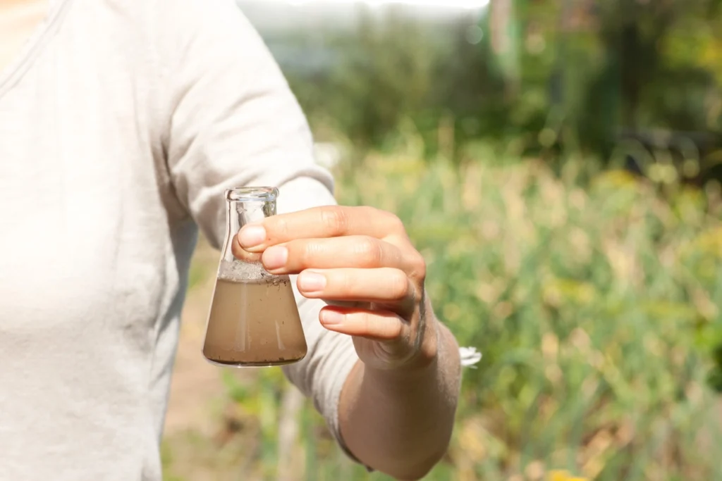 man holding a glass beaker with dirty groundwater