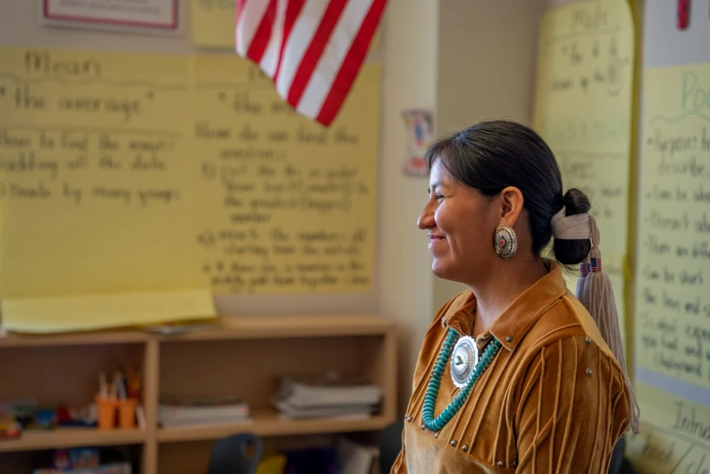 a native American wearing brown clothes, a large earring, and teal necklace