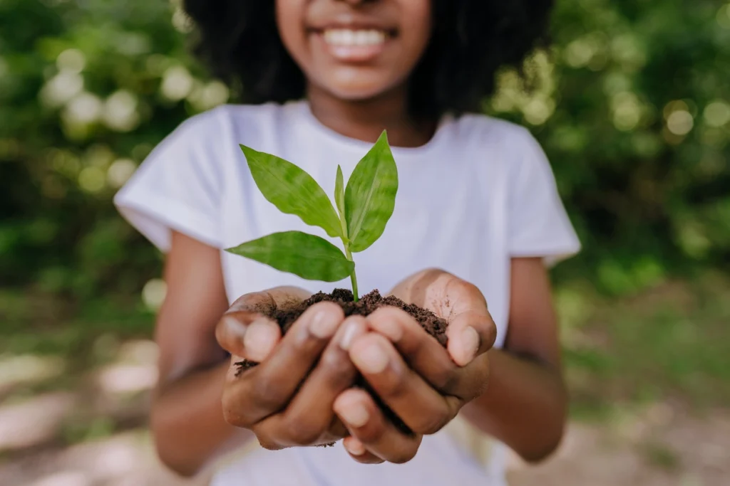 young black girl holding soil with a plant in the middle