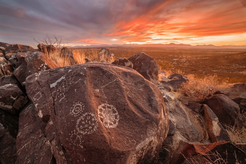 cultural site showing a rock with markings, a mountain range, and a sunset