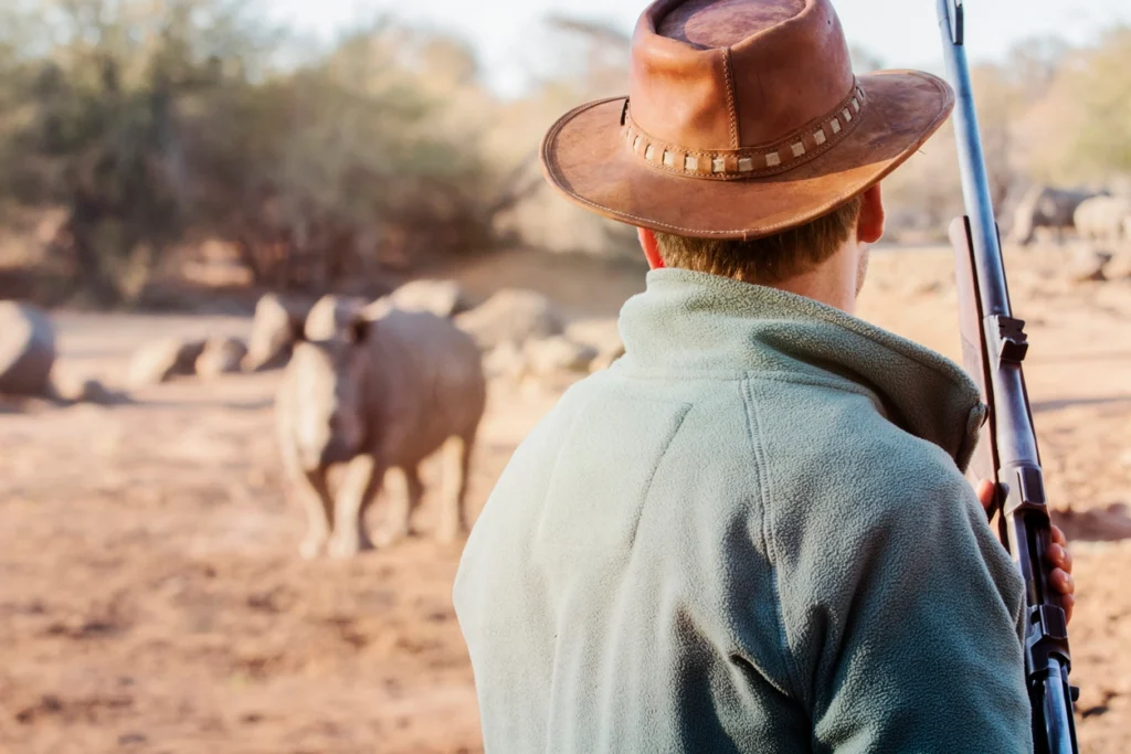 a man holding a gun in front of a rhinoceros; poaching